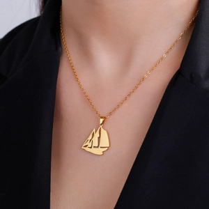 Collar con colgante de velero en acero inoxidable dorado usado por modelo sobre traje negro