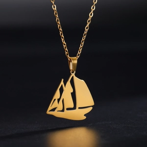 Detalle del colgante de velero dorado con diseño calado sobre fondo negro mate