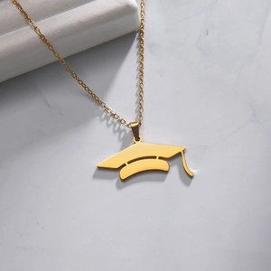 Detailed view of a gold graduation cap pendant on white marble texture background