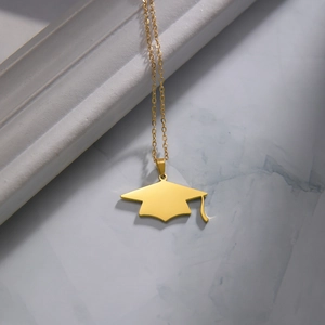 Detailopname van gouden afstudeerhoed hanger met kwastje aan een fijne ketting