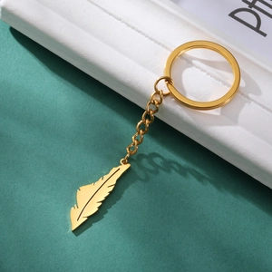 Polished gold stainless steel feather keychain pendant with a sleek link chain on stone background