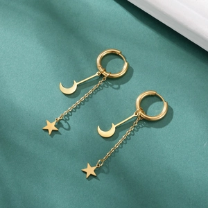 Détail de boucles d'oreilles dorées avec pendentif étoile et lune sur fond vert foncé