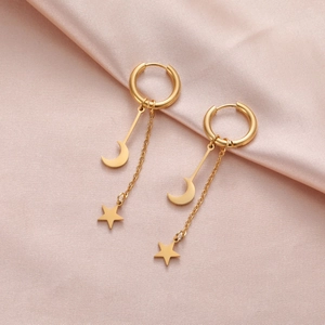 Détail de boucles d'oreilles créoles avec étoiles et lunes sur tissu de satin rose