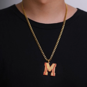 Détail du pendentif lettre M dorée avec coutures de baseball rouges sur chaîne cubaine