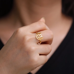 Détail d'une bague zodiaque dorée avec croissant de lune et signe Gémeaux portée au doigt