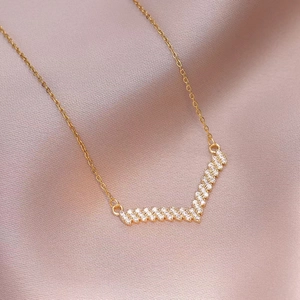 Elegante collar con colgante en V dorado y circonitas micropavé sobre fondo seda rosa