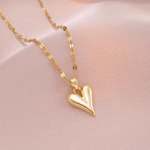 Elegant gold heart pendant necklace with polished mirror finish on pink velvet background