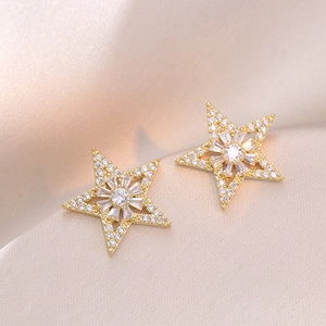 Eleganti orecchini a stella dorati con zirconi su sfondo di seta color champagne