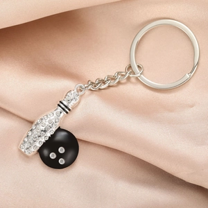 Porte-clés quille de bowling argenté avec strass et boule noire sur fond en satin