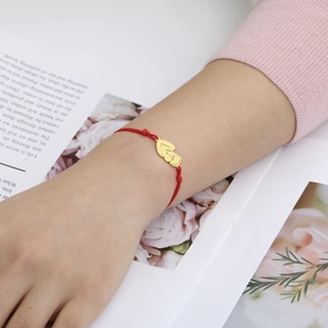 Red braided cord bracelet with a golden double heart pendant on a floral background