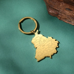 Detail view of gold Punjab map keychain with laser engraved city names on wood background