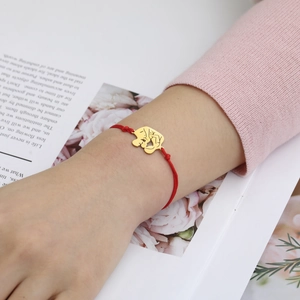 Detail of red woven cord bracelet with gold charm worn with floral background