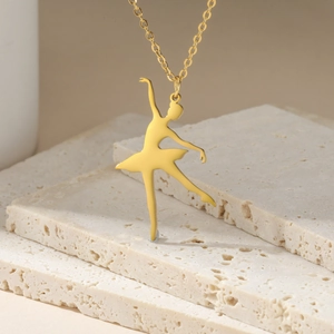 Detailed close-up of a golden ballet dancer pendant on a delicate cross chain necklace