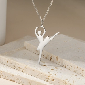 Detailed view of silver ballet dancer pendant on a delicate chain over travertine