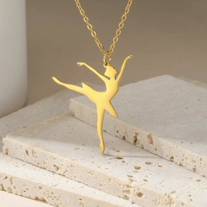 Detail view of a gold ballet dancer pendant on a cross chain against natural stone