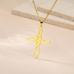 Gros plan d'un pendentif croix à nœud celtique doré avec chaîne fine sur pierre beige
