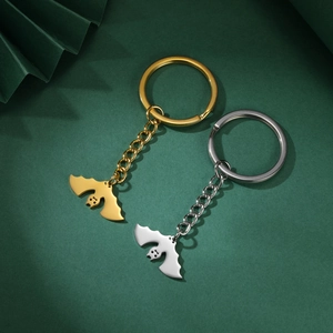 Detail of silver and gold bat-shaped keychains with polished finish on a green background