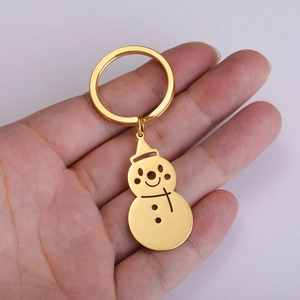 Close-up of hand holding a golden snowman keychain with detailed hat and bow design