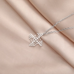 Detailed close-up of geometric windmill pendant on stainless steel chain over silk fabric
