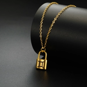 Detalle macro de un collar con colgante de candado dorado y signo de Géminis grabado