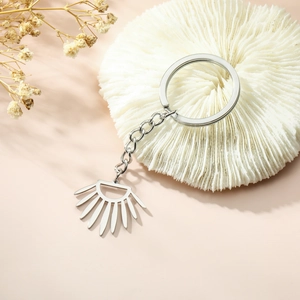 Minimalist silver stainless steel geometric keychain with sunburst pendant on marble base