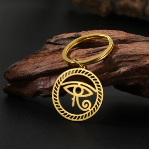Golden stainless steel Eye of Horus keychain on a dark wood background with a rustic look