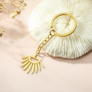 Polished gold stainless steel key ring with a geometric sunburst fan pendant on a white tray