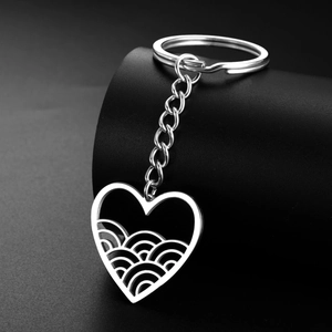 Macro detail of silver stainless steel heart keychain with wave pattern on dark background