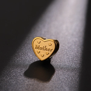 Macro view of a heart-shaped gold-plated bead featuring Mother engraving and tiny embossed hearts