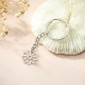 Polished stainless steel daisy cutout keychain with a chain link on a soft pink background