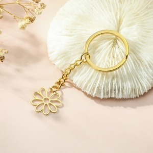 Gold hollow daisy pendant keychain on a white coral texture display stand