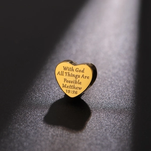 Polished gold heart charm with engraved Bible verse Matthew 19:26 on black sand background