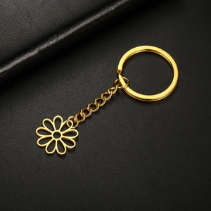 Detail of a golden hollow flower keychain with short chain on black leather background