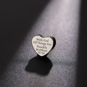 Macro detail of heart charm with engraved Bible verse Matthew 19:26 on polished steel