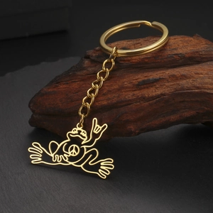 Detail of a golden frog keychain with peace sign and love gesture on a stone base