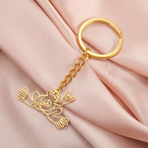 Close-up of golden stainless steel hollow peace frog keychain on pink satin background