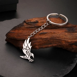 Macro detail of silver raven pendant keychain on wood and stone textured background