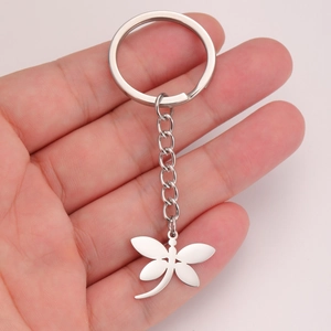 Polished silver stainless steel dragonfly keychain held by hand against a pale background