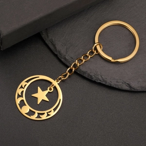 Close-up of golden stainless steel pentagram moon phase keychain on dark background