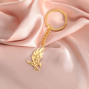 Close-up of golden stainless steel eagle pendant keychain on smooth pink silk fabric