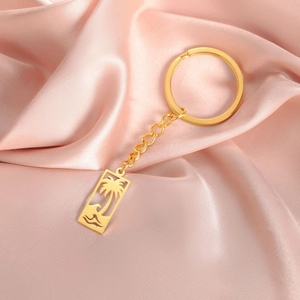 Gros plan d'un porte-clés doré avec pendentif palmier et vague sur du tissu en soie rose