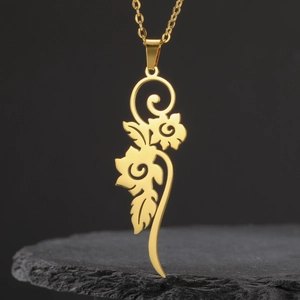 Collar largo de acero inoxidable dorado con colgante de flor hueca sobre una roca oscura