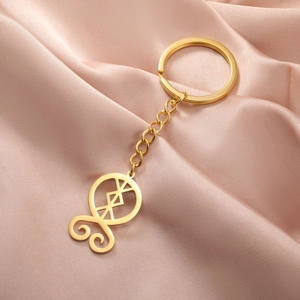 Detailed macro view of the golden hollow troll cross keychain on soft pink satin fabric