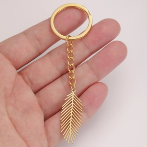 Detailed close-up of a gold stainless steel leaf pendant on a keychain held by hand