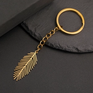 Macro shot of minimalist gold leaf pendant keychain on a dark textured rock background