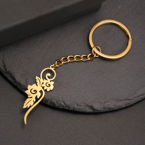 Close-up of golden stainless steel keychain with hollow floral pendant on slate tray