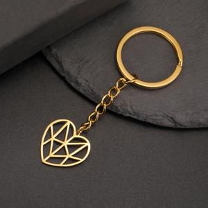 Detailed view of a gold geometric heart pendant keychain on a luxury black stone background