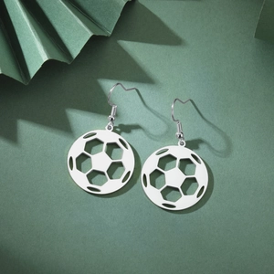 Close-up of stainless steel soccer ball earrings with hollow geometric pattern on green background