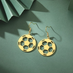 Close-up of golden hollow soccer ball dangle earrings on a dark green textured surface