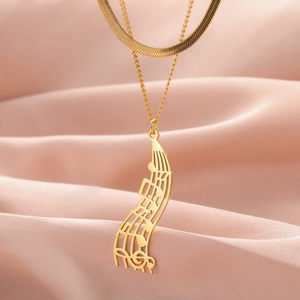 Close-up of golden layered music note necklace with sheet music charm on pink silk